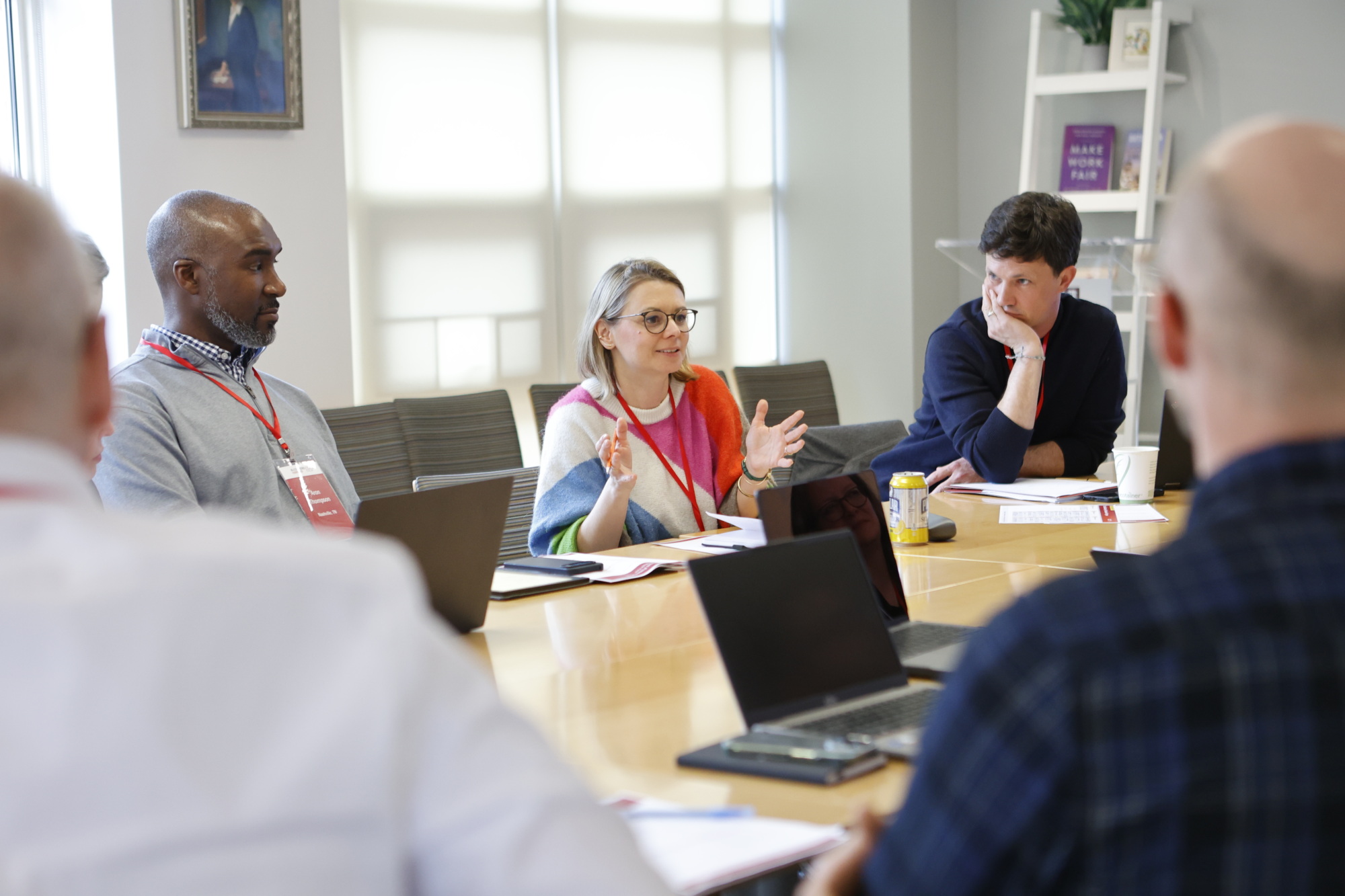 Group of people working at a table listening to a woman talk