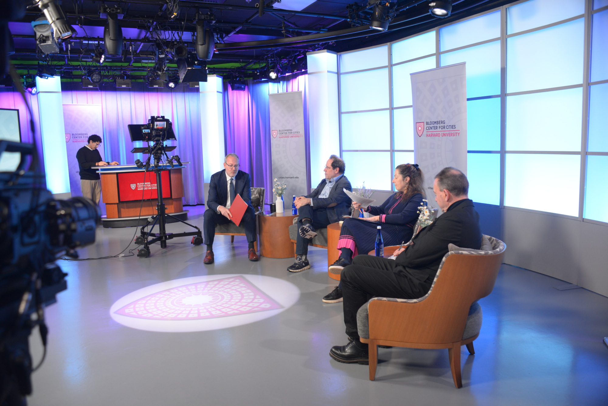 People on panel preparing for their recorded discussion with camera in the background and crew